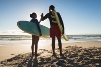 Glückliches afrikanisch-amerikanisches Paar am Strand mit Surfbrettern hoch fünf. gesunde Freizeit im Freien am Meer. — Stockfoto