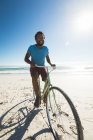 Happy african american man on beach riding bicycle. healthy outdoor leisure time by the sea. — Stock Photo