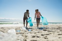 Glückliches afrikanisch-amerikanisches Paar, das Latex-Handschuhe trägt und Müll am Strand sammelt. Öko-Strandschutz im Sommer — Stockfoto
