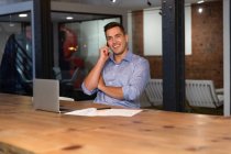 Porträt eines glücklichen kaukasischen Geschäftsmannes, der am Schreibtisch mit dem Smartphone spricht. Geschäftsmann bei der Arbeit im modernen Büro. — Stockfoto
