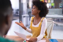 Glückliche afrikanisch-amerikanische Geschäftsfrau hält Dokument in der Hand und spricht mit Kollegen im Besprechungsraum. unabhängiges kreatives Designgeschäft. — Stockfoto