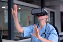 Caucasian female doctor wearing scrubs using vr headset and virtual interface. medical professional at work with technology. — Stock Photo