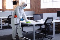 Cleaner wearing hygiene overalls, gloves and face mask disinfecting office and furniture. business workplace hygiene during coronavirus covid 19 pandemic. — Stock Photo