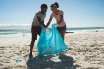 Glückliches afrikanisch-amerikanisches Paar, das Latex-Handschuhe trägt und Müll am Strand sammelt. Öko-Strandschutz im Sommer — Stockfoto