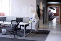 Limpador vestindo macacões de higiene, luvas e máscara facial desinfectando escritório e móveis. higiene no local de trabalho durante a pandemia do coronavírus covid 19. — Fotografia de Stock