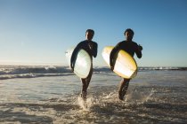 Glückliches afrikanisch-amerikanisches Paar, das mit Surfbrettern aufs Meer rennt. gesunde Freizeit im Freien am Meer. — Stockfoto