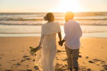 Afroamerikanisches verliebtes Paar, das bei Sonnenuntergang Händchen haltend am Strand spaziert. Liebe, Romantik und Hochzeit Strandurlaub Sommerurlaub. — Stockfoto