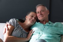 Feliz pareja de ancianos caucásicos relajarse en la sala de estar sentado en el sofá abrazando y sonriendo. permanecer en casa aislado durante el bloqueo de cuarentena. - foto de stock