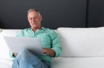 Heureux homme âgé caucasien assis dans le salon regardant ordinateur portable et souriant. rester à la maison dans l'isolement pendant le confinement en quarantaine. — Photo de stock