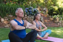 Happy caucasian senior couple in garden practicing yoga, sitting and meditating. staying at home in isolation during quarantine lockdown. — Stock Photo