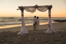 Африканська пара закоханих в одруження, гуляючи на пляжі під час заходу сонця, тримаючись за руки. Любов, романтика і весільне узбережжя перерва літніх канікул. — стокове фото