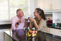 Glückliches kaukasisches Seniorenpaar in der Küche, das an der Insel sitzt, Kaffee trinkt und sich unterhält. Isolationshaft während der Quarantäne. — Stockfoto