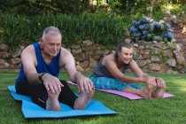 Щаслива кавказька старша пара займається в саду, сидячи на килимках, що практикують йогу. перебування вдома в ізоляції під час карантину . — стокове фото