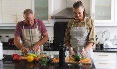 Glückliches kaukasisches Seniorenpaar in der Küche, das Schürzen trägt und gemeinsam Essen zubereitet. Isolationshaft während der Quarantäne. — Stockfoto