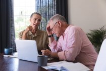 Concerned caucasian senior couple in living room at table using laptop, doing paperwork and talking. staying at home in isolation during quarantine lockdown. — Stock Photo
