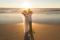 Afroamerikanisches verliebtes Paar, das sich bei Sonnenuntergang am Strand umarmt. Liebe, Romantik und Hochzeit Strandurlaub Sommerurlaub. — Stockfoto