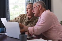 Surprised caucasian senior couple in living room at table using laptop, paying bills and talking. staying at home in isolation during quarantine lockdown. — Stock Photo