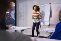 Mixed race businesswoman standing at whiteboard giving presentation to diverse group of colleagues. independent creative design business. — Stock Photo