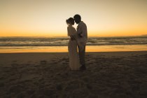 Feliz pareja afroamericana enamorada de casarse, abrazándose en la playa al atardecer. amor, romance y boda vacaciones de verano vacaciones de playa. - foto de stock
