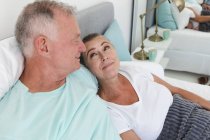 Happy caucasian senior couple relaxing in bedroom, sitting up in bed and smiling at each other. staying at home in isolation during quarantine lockdown. — Stock Photo