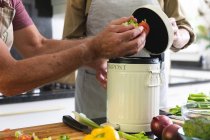 Sezione centrale di anziani caucasici in cucina che indossano grembiuli che mettono rifiuti organici nel bidone del compost. stare a casa in isolamento durante la quarantena. — Foto stock