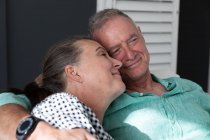 Щаслива кавказька старша пара розслабляється у вітальні, сидячи на дивані, обіймаючись і посміхаючись. перебування вдома в ізоляції під час карантину . — стокове фото