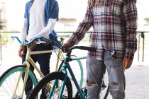 Sección media de dos amigos machos de raza mixta que ruedan bicicletas en la calle. estilo de vida urbano verde, fuera y alrededor de la ciudad. - foto de stock