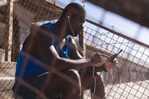 African american man exercising, wearing headphones, using smartphone on sunny day. healthy outdoor lifestyle fitness training. — Photo de stock