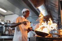 Afrikanische männliche Profikoch Flammengericht im Wok. Arbeit in einer belebten Restaurantküche. — Stockfoto