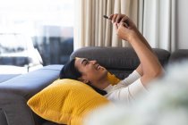 Счастливая трансгендерная расовая женщина отдыхает в гостиной, лежа на диване, делая селфи. оставаться дома в изоляции во время карантинной изоляции. — стоковое фото