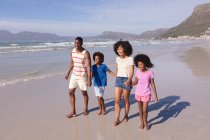 Afrikanisch-amerikanische Eltern und zwei Kinder lächeln, gehen und halten Händchen am Strand. Familienfreizeit im Freien am Meer. — Stockfoto