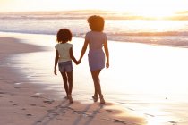 Африканская американская мать и дочь ходят и держатся за руки на пляже. здоровый отдых на открытом воздухе у моря. — стоковое фото