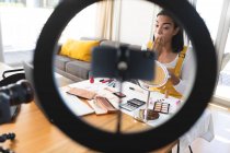 Mixed race transgender woman making vlog using laptop, smartphone and lighting putting on makeup. staying at home in isolation during quarantine lockdown. — Stock Photo