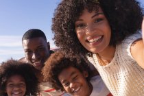 African american parents and two children taking a selfie with smartphone at the beach smiling. family outdoor leisure time by the sea. — Foto stock