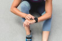 Midsection of woman checking smartwatch preparing for climb at indoor climbing wall. fitness and leisure time at gym. — Stock Photo