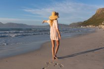 Kaukasische Frau mit Strandkleidung und Hut, die Spaß am Spazierengehen am Strand hat. gesunde Freizeit im Freien am Meer. — Stockfoto