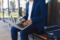 Mezzo sezione di maschio seduto sulla panchina in strada utilizzando il computer portatile. nomade digitale, in giro per la città. — Foto stock