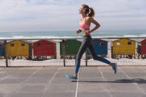 Mulher caucasiana exercitando jogging em um passeio pela praia. tempo de lazer ao ar livre saudável pelo mar. — Fotografia de Stock