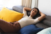 Счастливая трансгендерная расовая женщина отдыхает в гостиной, лежа на диване. оставаться дома в изоляции во время карантинной изоляции. — стоковое фото