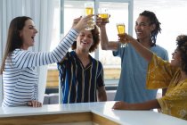 Diverso grupo de colegas masculinos y femeninos que levantan vasos de cerveza en el bar. amigos socializando y bebiendo en el bar. - foto de stock