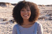 Portrait of african american woman looking at camera and smiling at the beach. healthy outdoor leisure time by the sea. - foto de stock