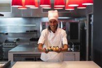 Portrait of mixed race professional chef wearing chefs hat serving sushi. chef at work in a modern restaurant kitchen. — Stock Photo