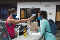 Женщина секретарша и клиент в масках проверяет температуру на прилавке в спортзале. фитнес и досуг в тренажерном зале во время коронавируса ковид 19 пандемии. — стоковое фото