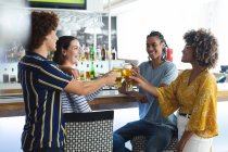 Diverse group of male and female colleagues raising glasses of beer at bar. friends socialising and drinking at bar. — Stock Photo