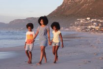 Afrikanisch-amerikanische Mutter und zwei Kinder beim Gehen und Händchenhalten am Strand. gesunde Freizeit im Freien am Meer. — Stockfoto
