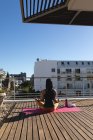 Вид ззаду змішаної раси трансгендерка, яка практикує медитацію йоги на терасі на сонці. перебування вдома в ізоляції під час карантину . — стокове фото