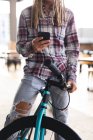 Ein Mann mit Dreadlocks sitzt auf einem Fahrrad auf der Straße und bedient das Smartphone. digitaler Nomade, unterwegs in der Stadt. — Stockfoto