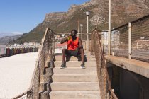 African american man exercising, resting, drinking water on stairs on sunny day. healthy outdoor lifestyle fitness training. — Stock Photo