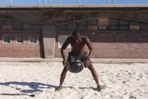 African american man exercising with weights on beach on sunny day. healthy outdoor lifestyle fitness training. — Fotografia de Stock