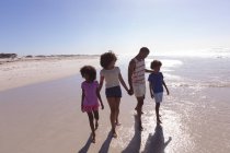 Батьки-афроамериканці і двоє дітей ходять і тримаються за руки на пляжі. сім'я на відкритому повітрі відпочиває біля моря. — стокове фото